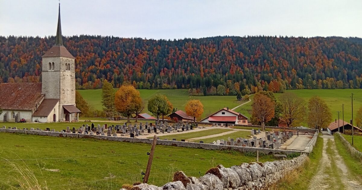 秋の森を背景にした田舎の教会と墓地の風景